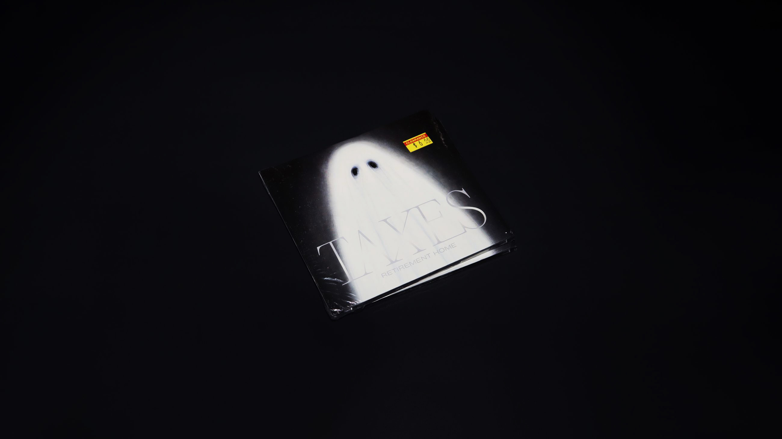 Photo of the CD angled at a distance on a back background. The CD cover has a painting of a ghost on it with the band name somewhat hidden in the fabric of the ghost 